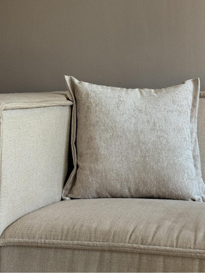 Beige fluwelen sierkussen met sierrand op een neutrale bank.