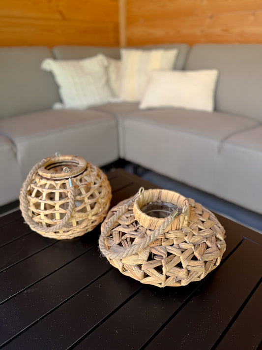 Gevlochten windlicht van waterhyacinth met een open structuur en hengsel.